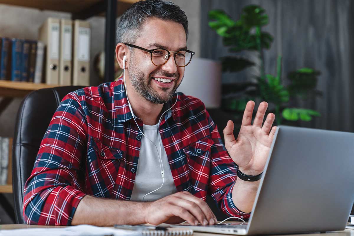 a man waves at his laptop camera while working one of the popular remote behavioral health jobs