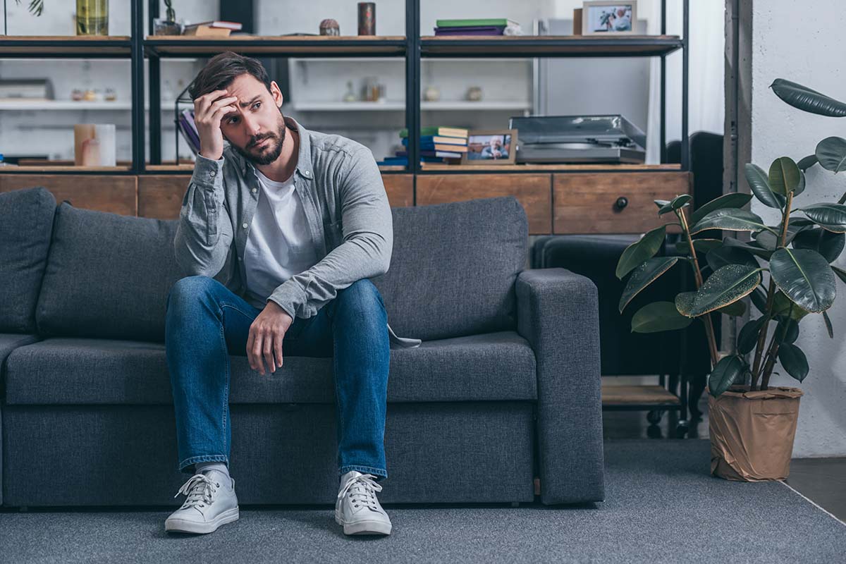 a person sadly sits on a couch possibly needing tips on how to deal with rejection from a job
